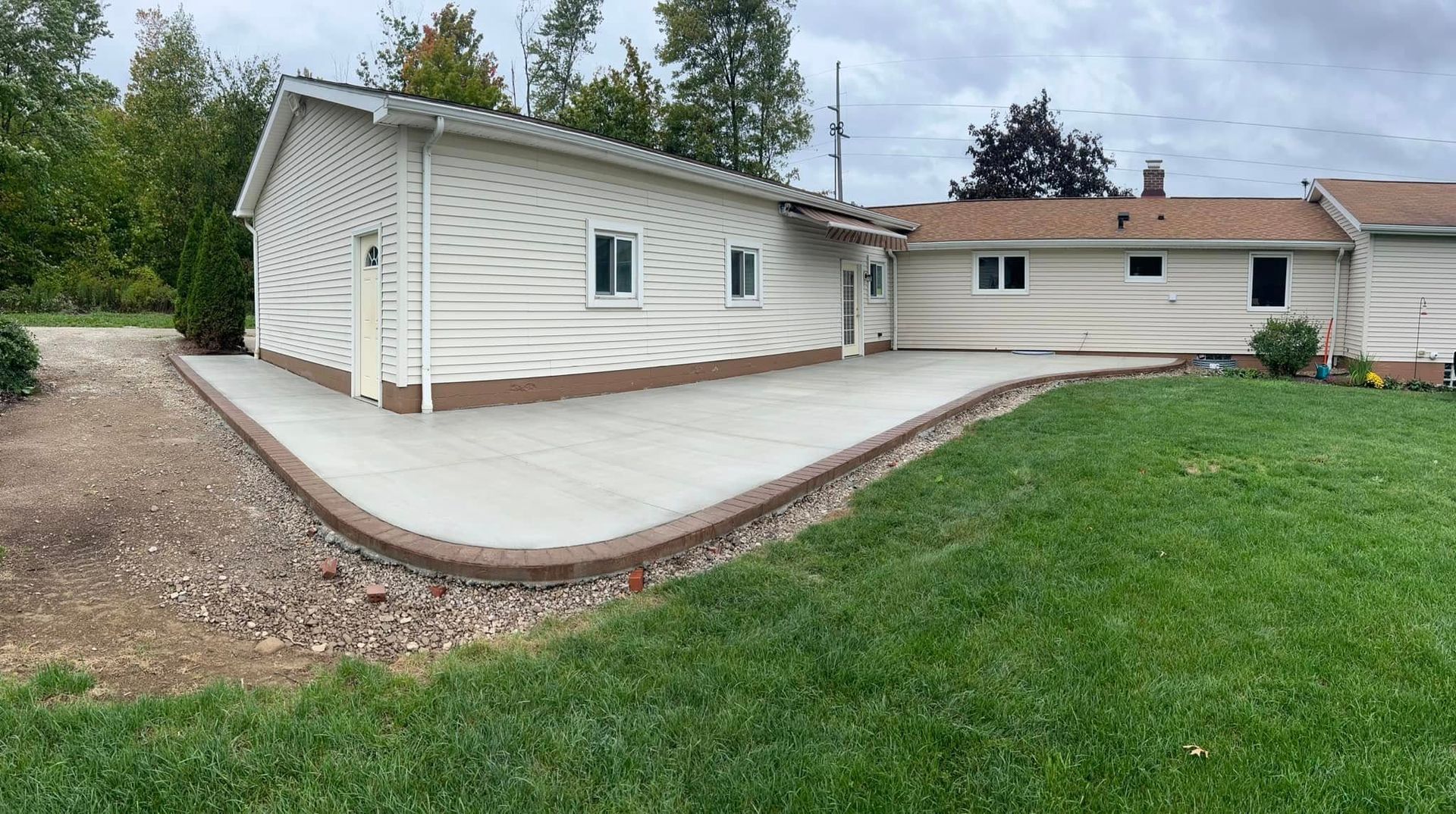 Concrete patio with brown border next to a house with beige siding and a green lawn.