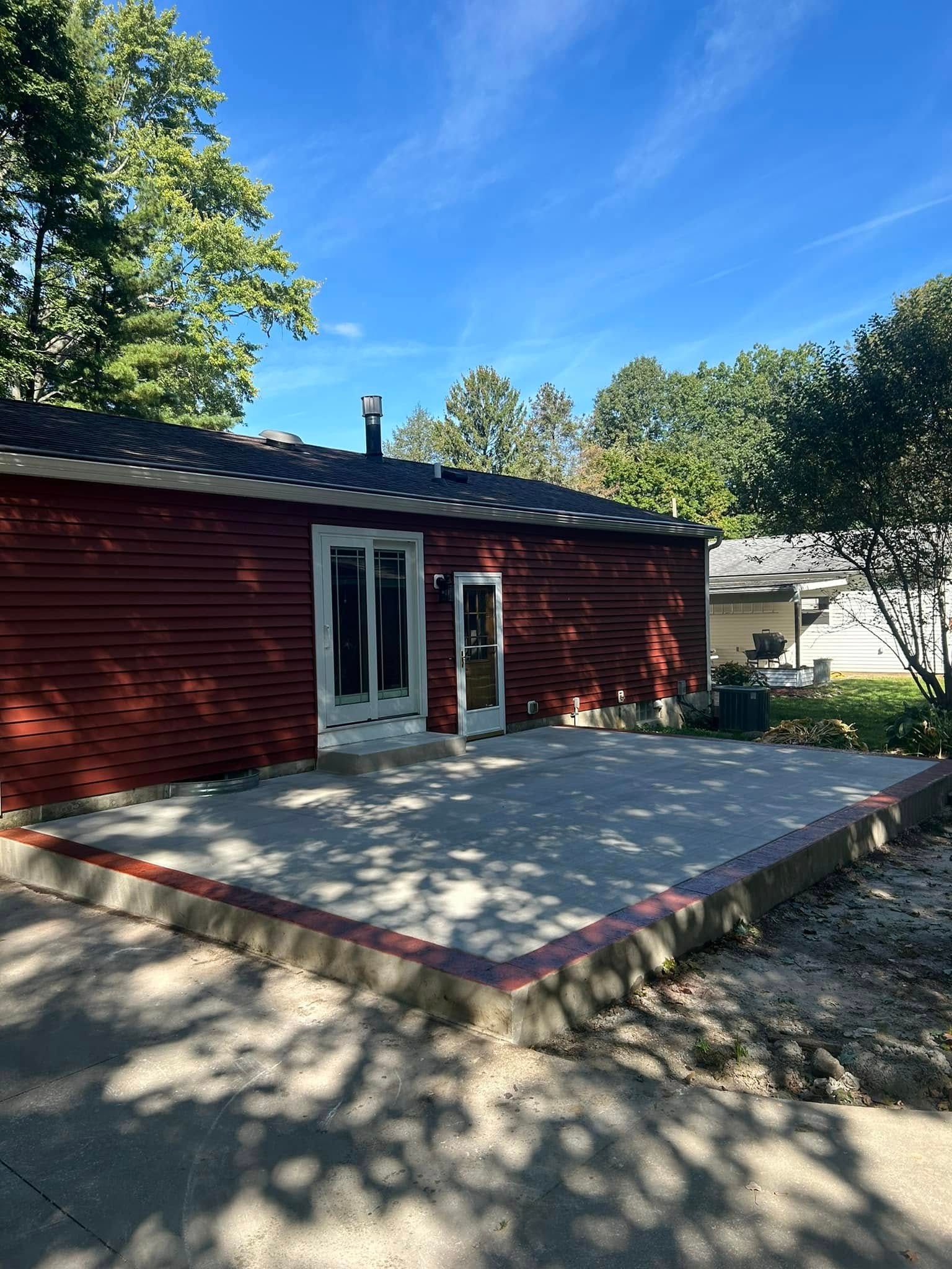 Red-sided building with patio, two doorways, and a concrete patio on a sunny day.