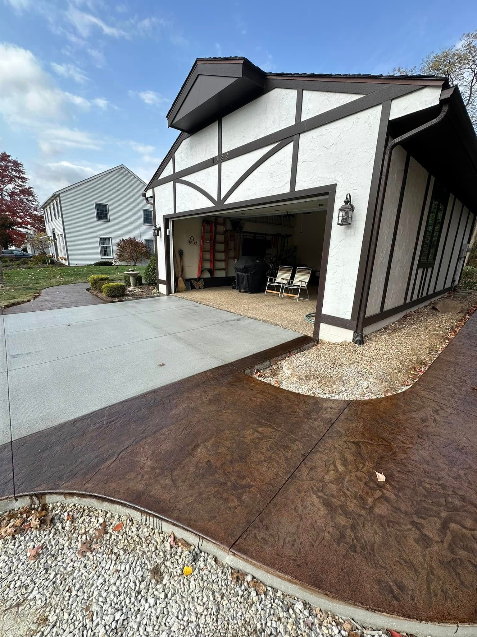 Tudor-style house with open garage and brown/gray driveway. White facade with brown trim and a light blue sky.