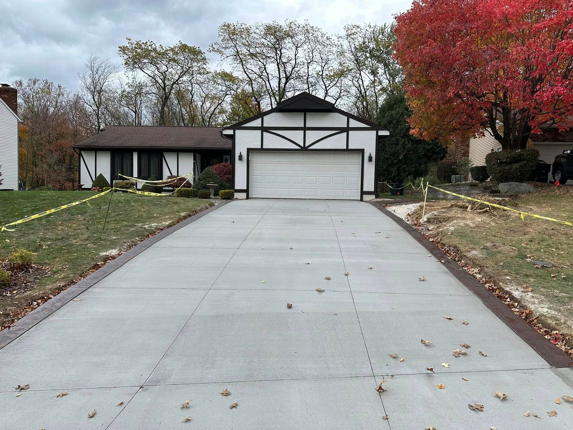 Newly poured concrete driveway leading to a house with a black and white facade and garage door, flanked by lawn.
