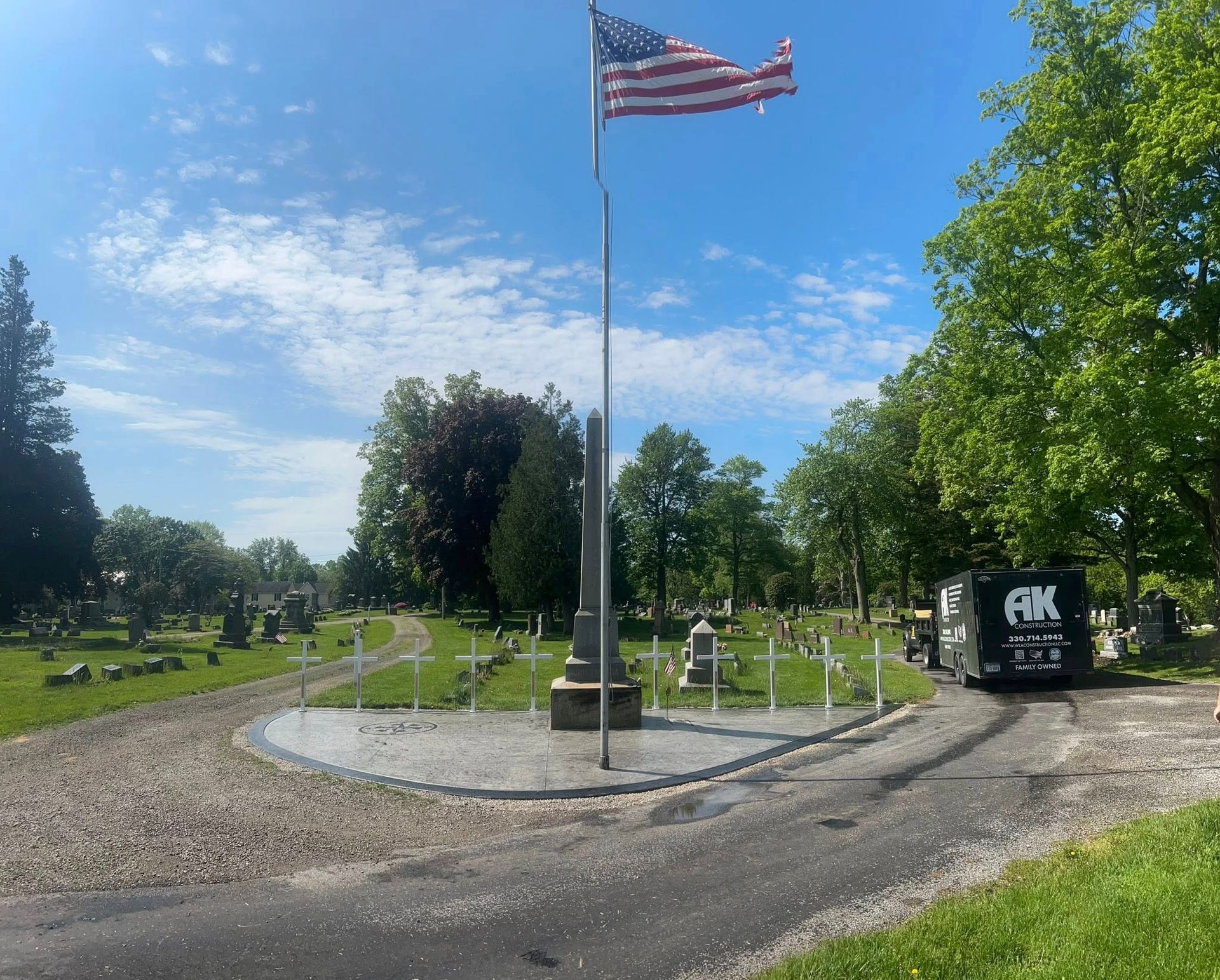 American flag flies over a cemetery with white crosses, vehicle to the right.
