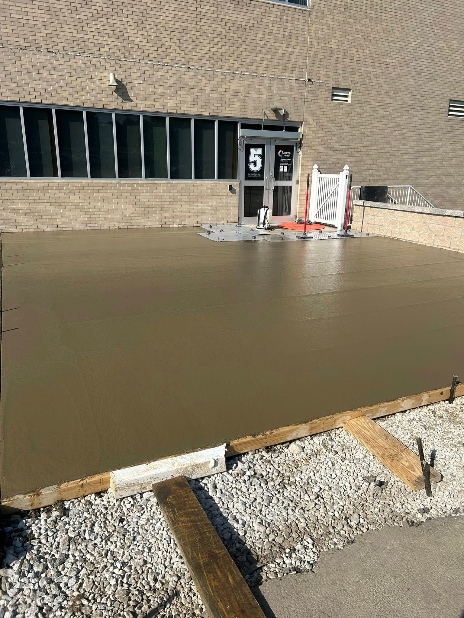 Freshly poured concrete in front of a building; forms and tools visible.