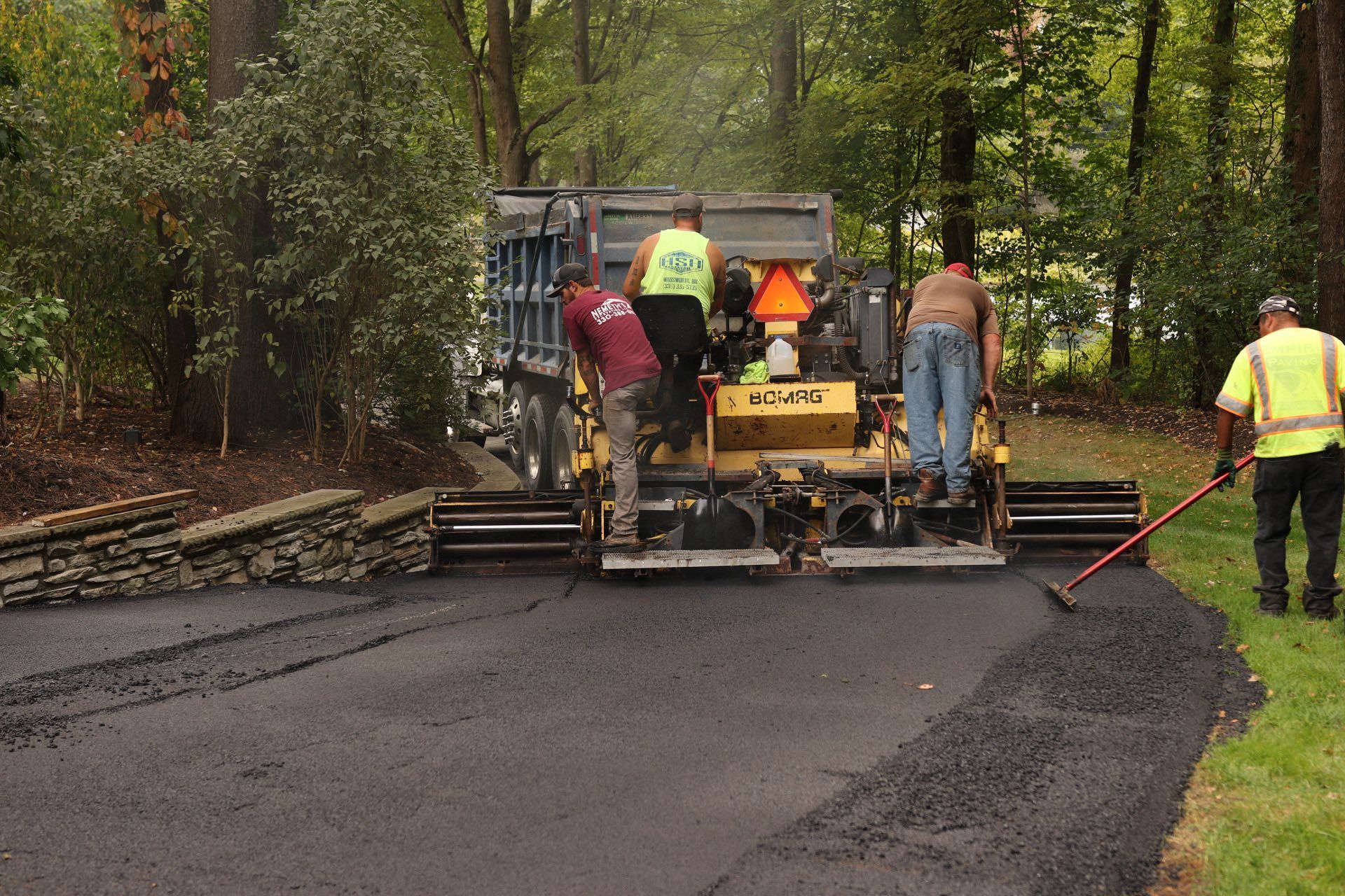 Asphalt paving crew laying black asphalt on a driveway; men raking and operating machinery.