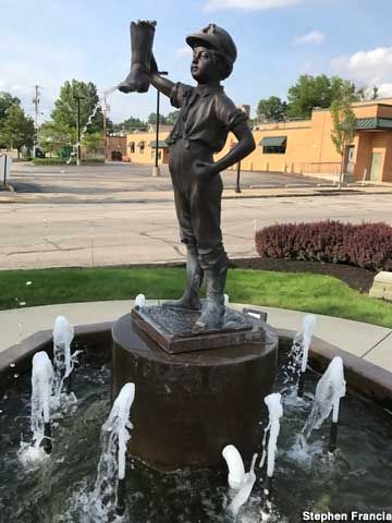 Bronze statue of a boy holding a boot above his head, standing on a fountain.
