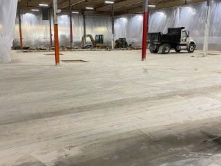 Interior of a construction site: dump truck, small excavator, and concrete floor. White plastic sheeting covers walls.