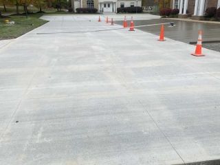 Newly poured concrete driveway with orange safety cones in a residential setting.