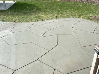 Gray concrete patio with geometric shapes and lines, on grass.