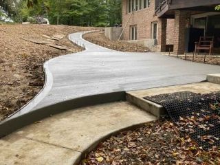 Newly poured concrete path curves uphill beside a brick house and landscaped areas.