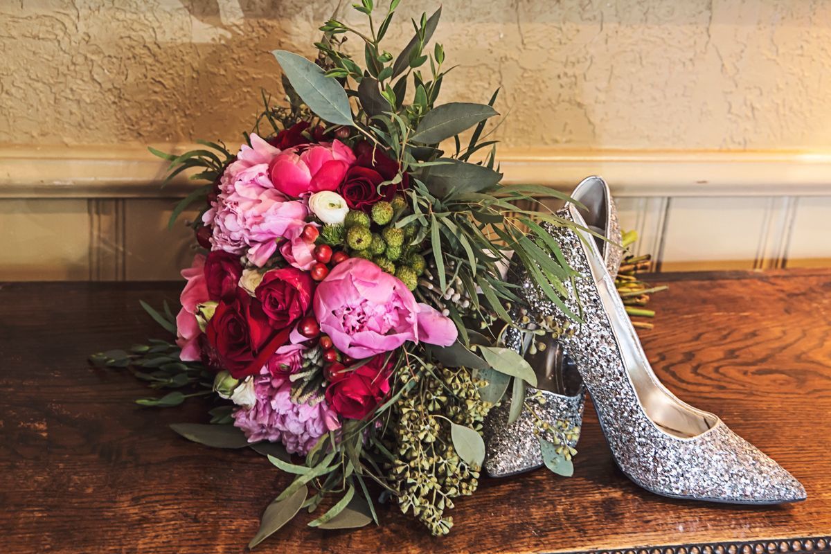 A bouquet of flowers and a pair of shoes are on a wooden table.