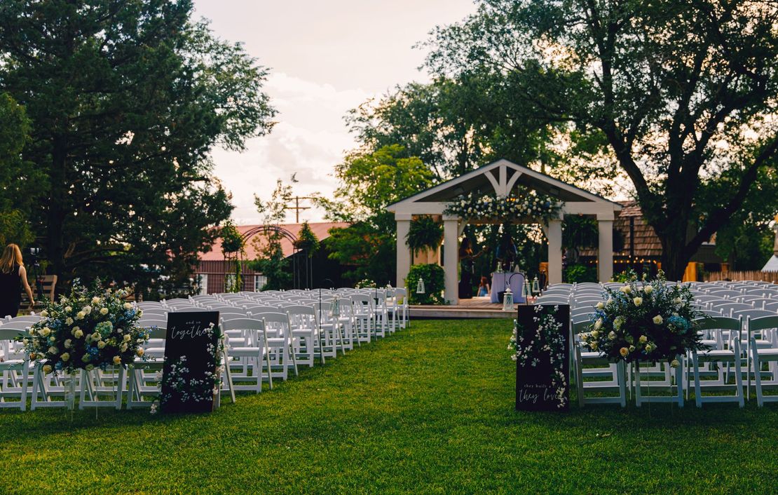 A white gazebo with flowers hanging from the columns in a park.