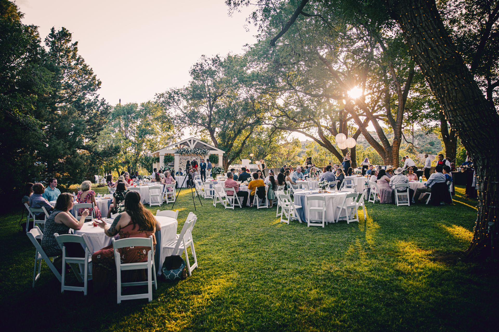 A large group of people are sitting at tables in a grassy field.