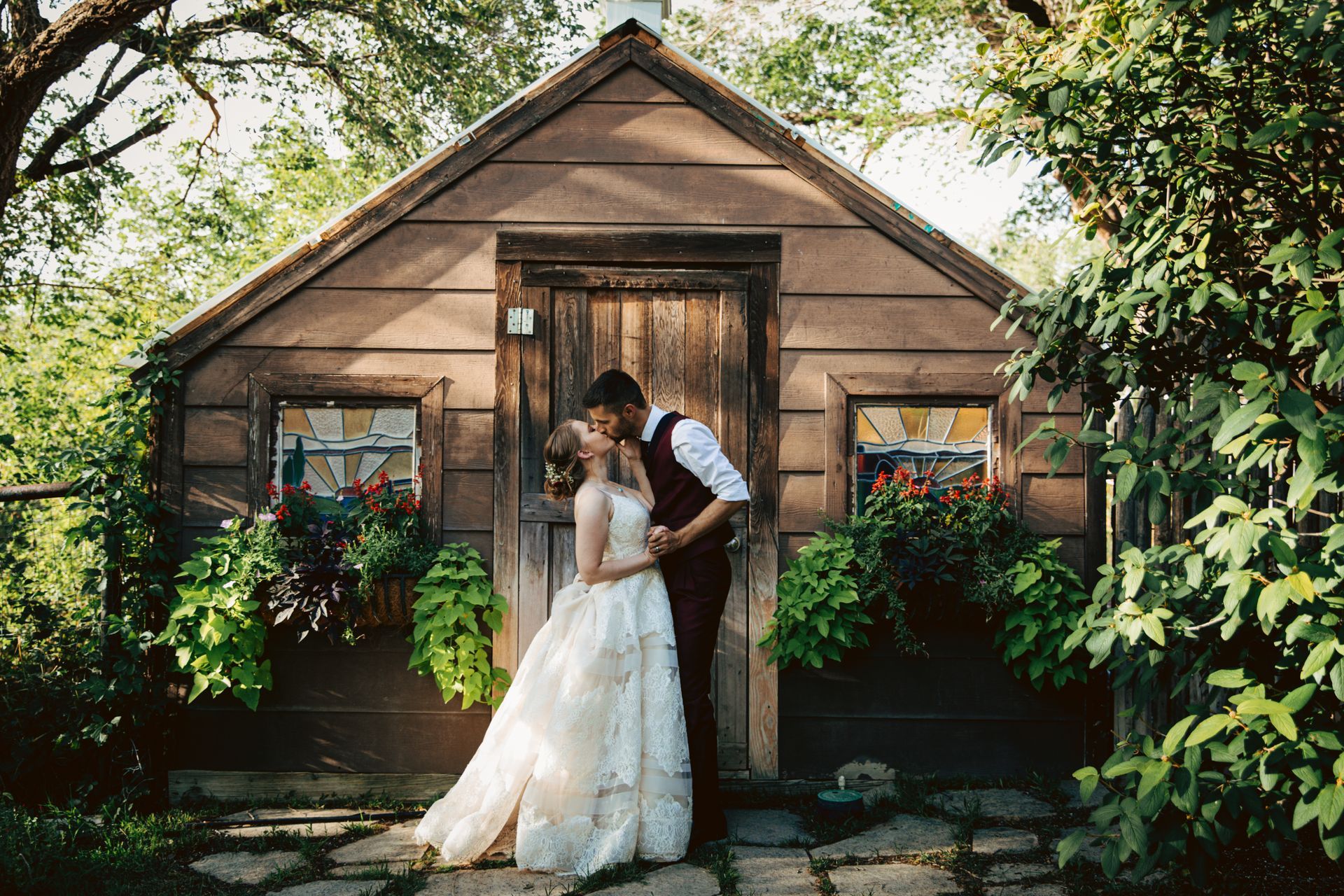 A bride and groom are kissing in front of a wooden building.