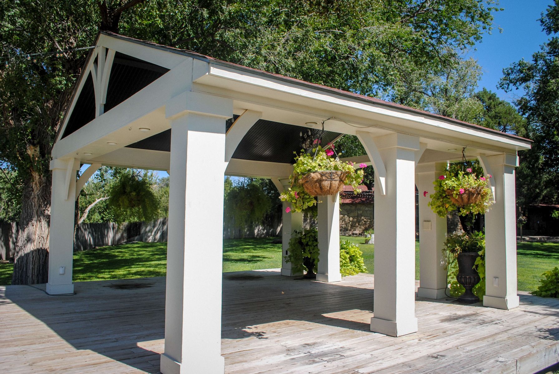 A white gazebo with flowers hanging from the columns in a park.