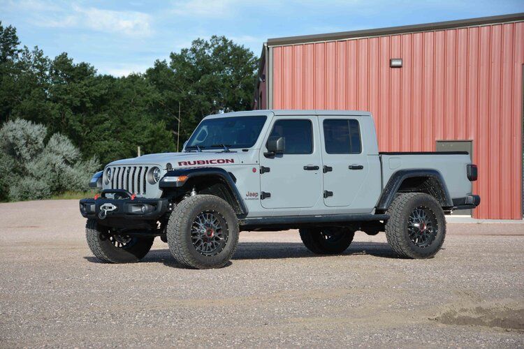 A gray jeep gladiator is parked in front of a red building.