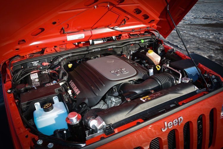 The engine of a red jeep is shown with the hood open.
