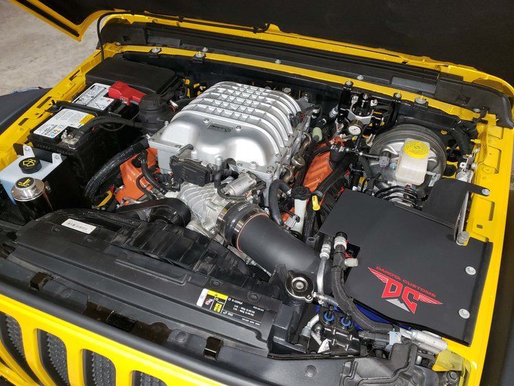 The engine of a yellow jeep is shown with the hood open.