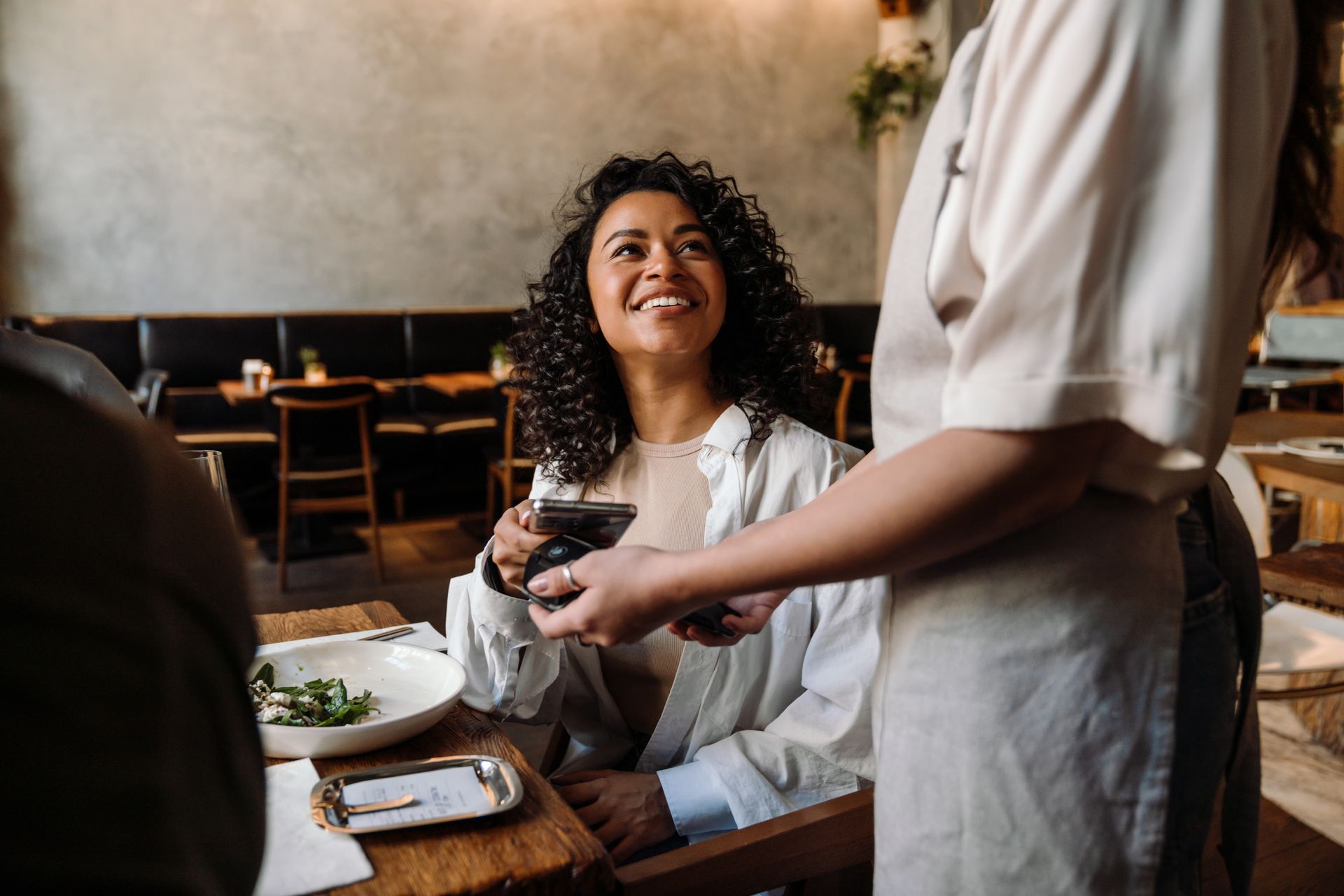 Woman smiles as a server hands her a drink at a restaurant table.