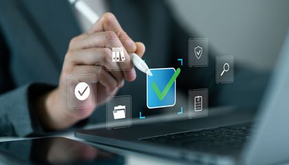 Person using a stylus to select a checkmark icon on a laptop screen, symbolizing approval.