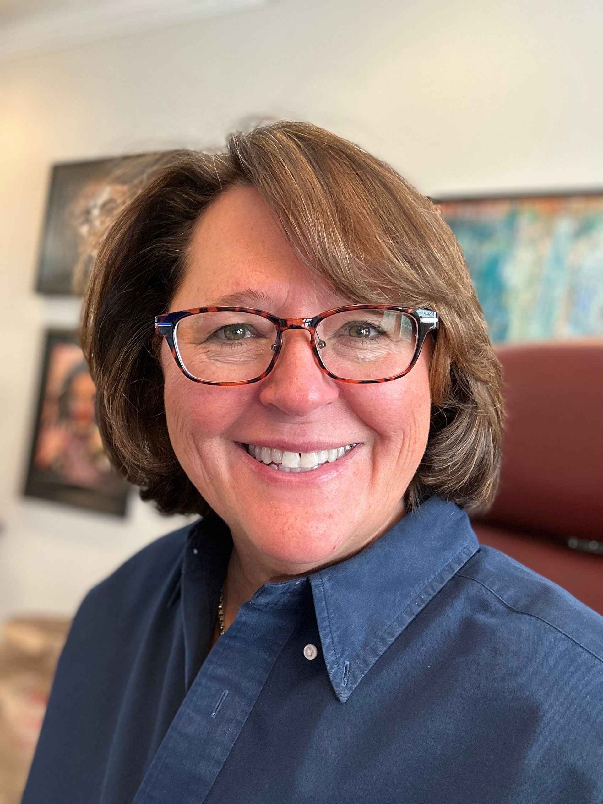 A woman wearing glasses and a blue shirt is smiling for the camera.