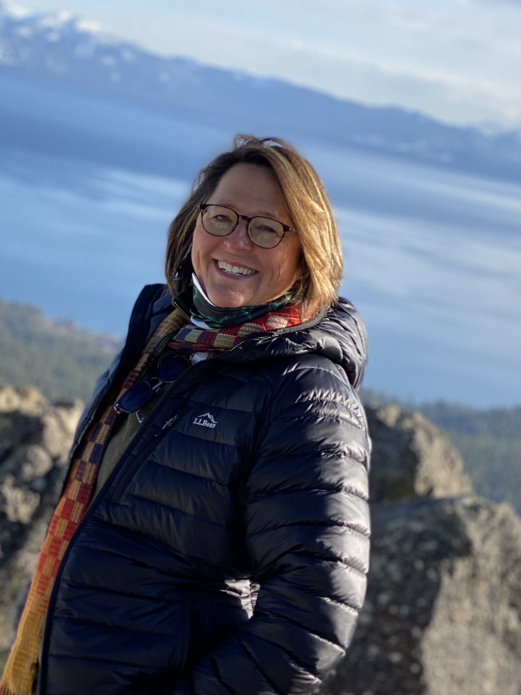 A woman in a black jacket and scarf is standing on top of a mountain.