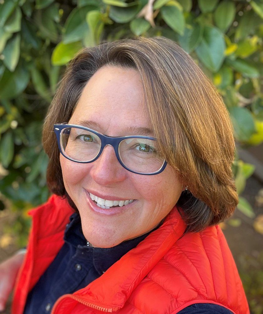A woman wearing glasses and a red vest is smiling for the camera.