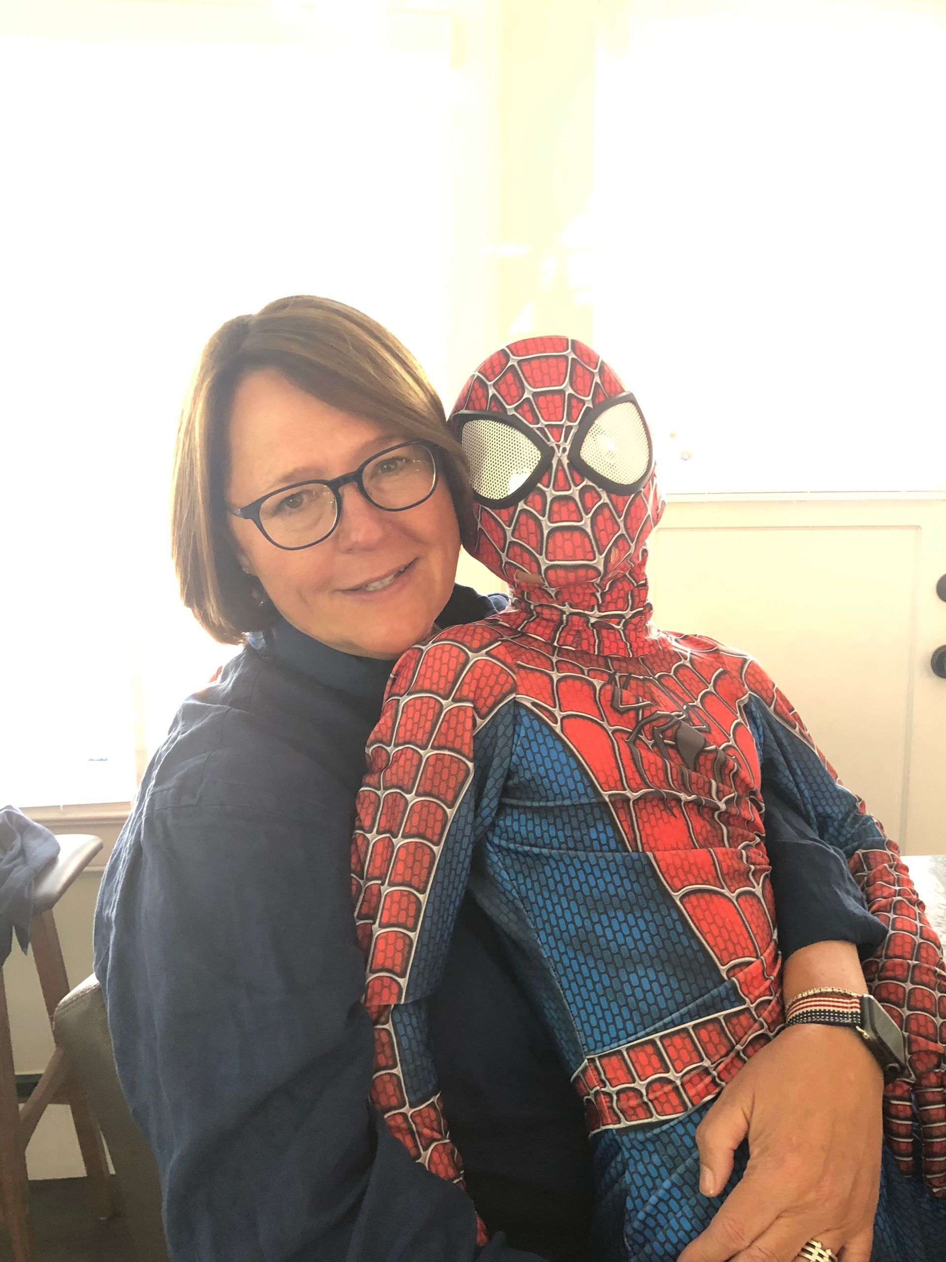 A woman is holding a child in a spiderman costume.