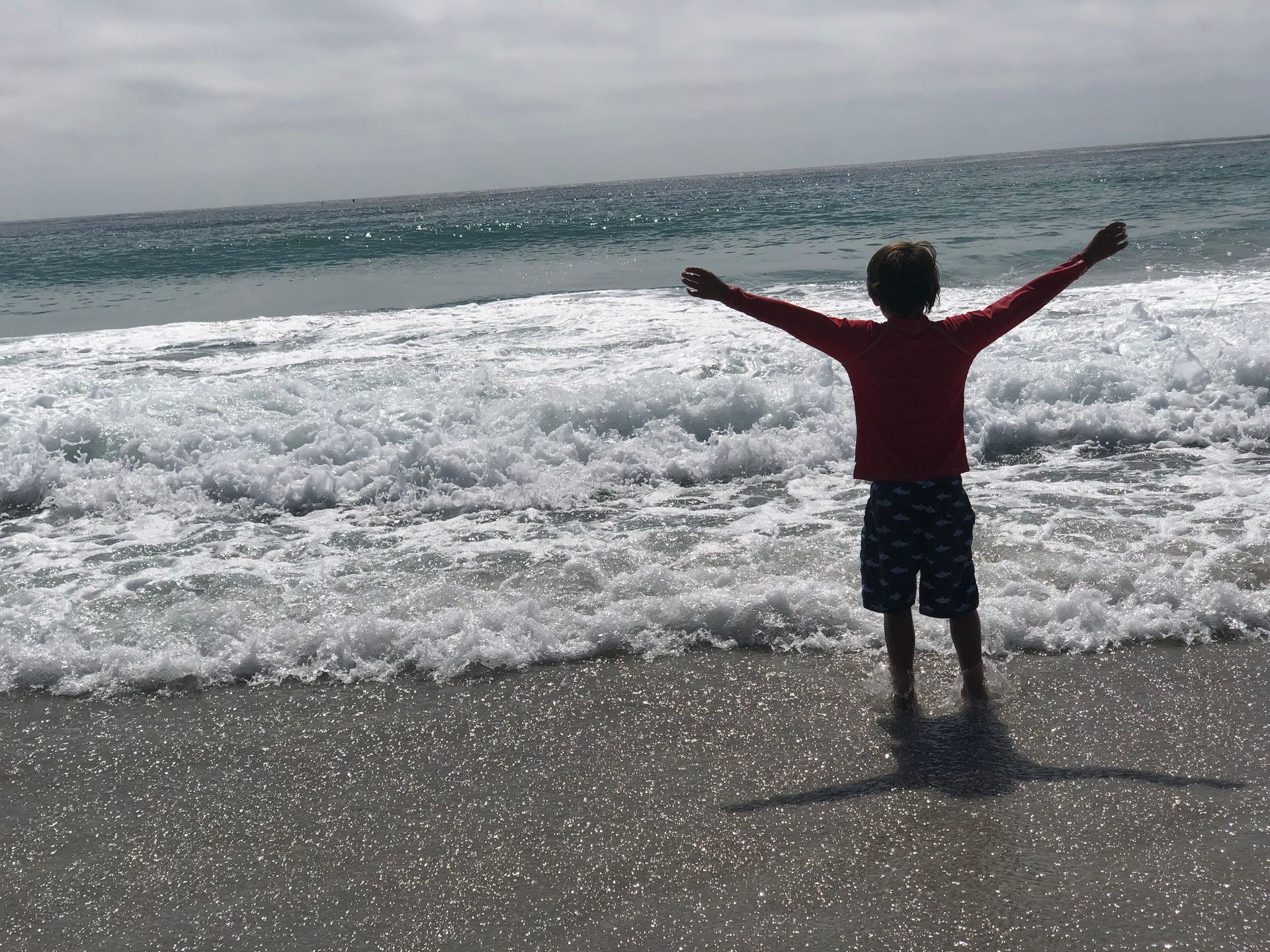 A young boy is standing on a beach with his arms outstretched.