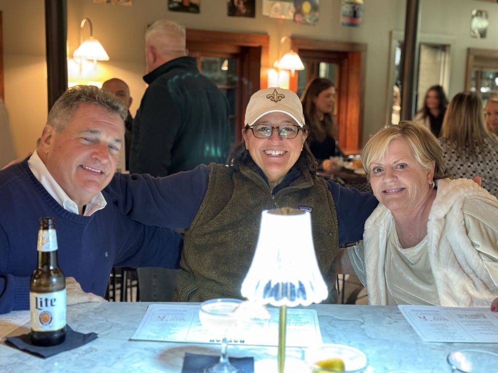 A man and two women are sitting at a table with a lite beer bottle on it.