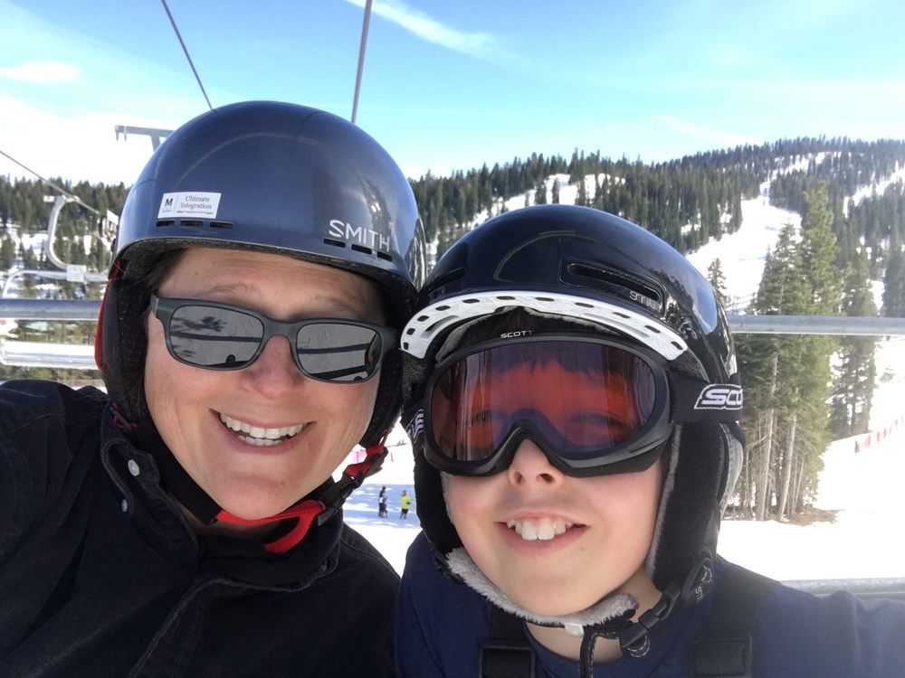 A woman and a child wearing ski helmets and goggles are posing for a picture.