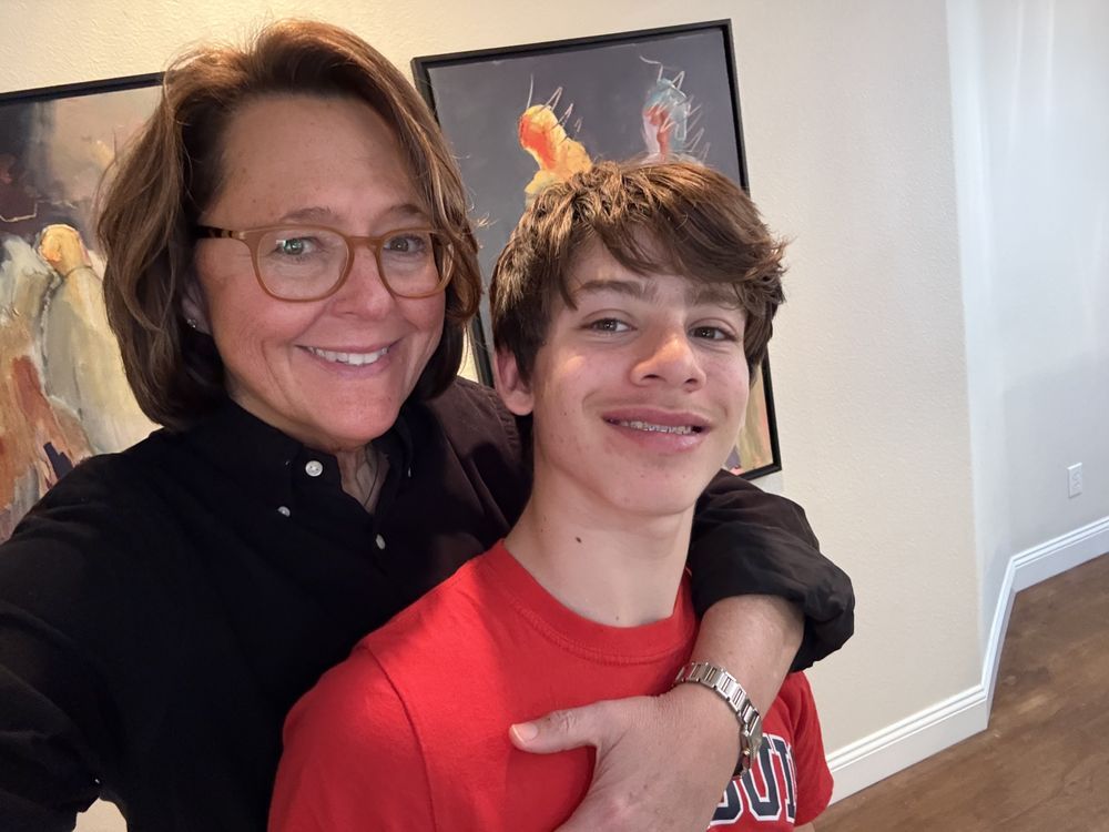 A woman is hugging a young boy in a red shirt.