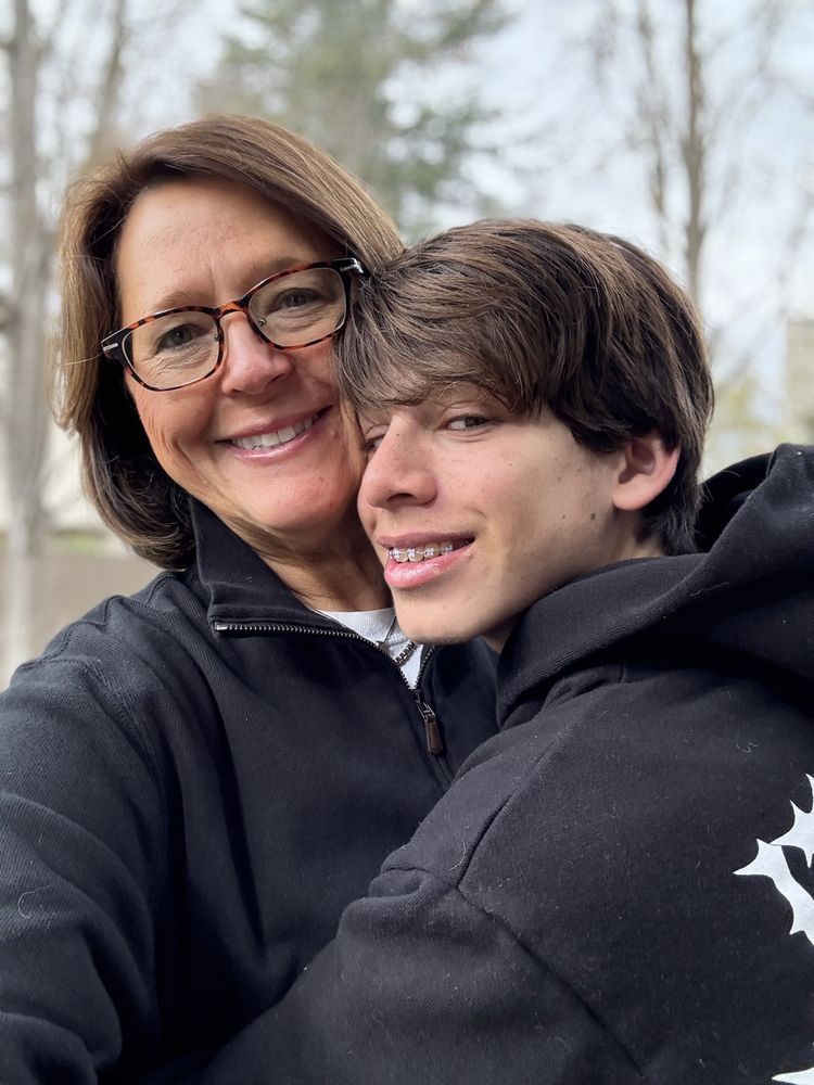 A woman wearing glasses is hugging a young boy wearing a black hoodie.