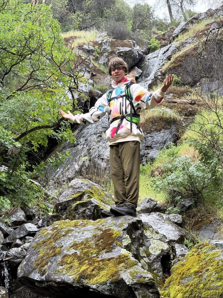 A man is standing on a rock in front of a waterfall.