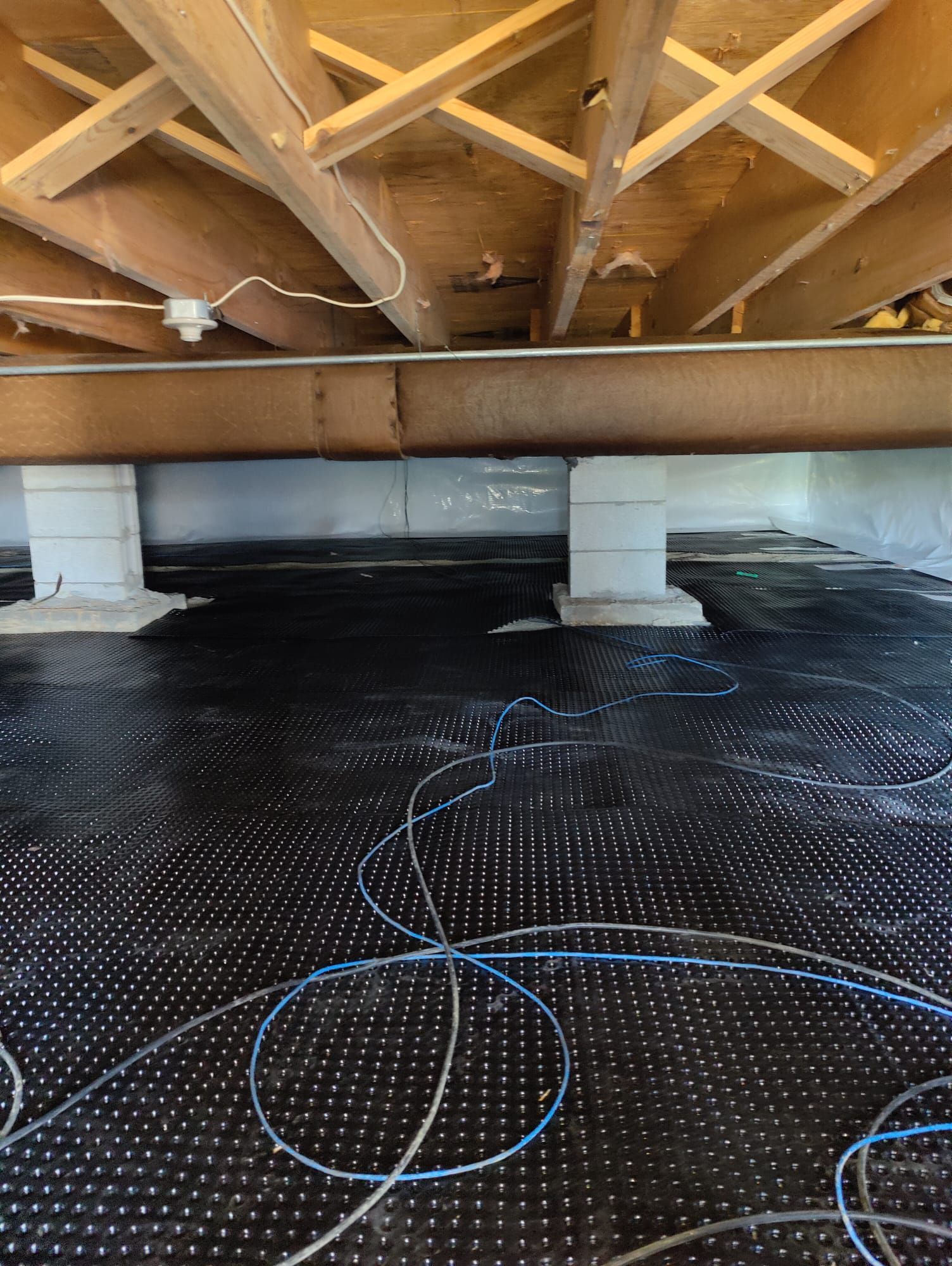 A crawl space under a house with a lot of wires on the floor.