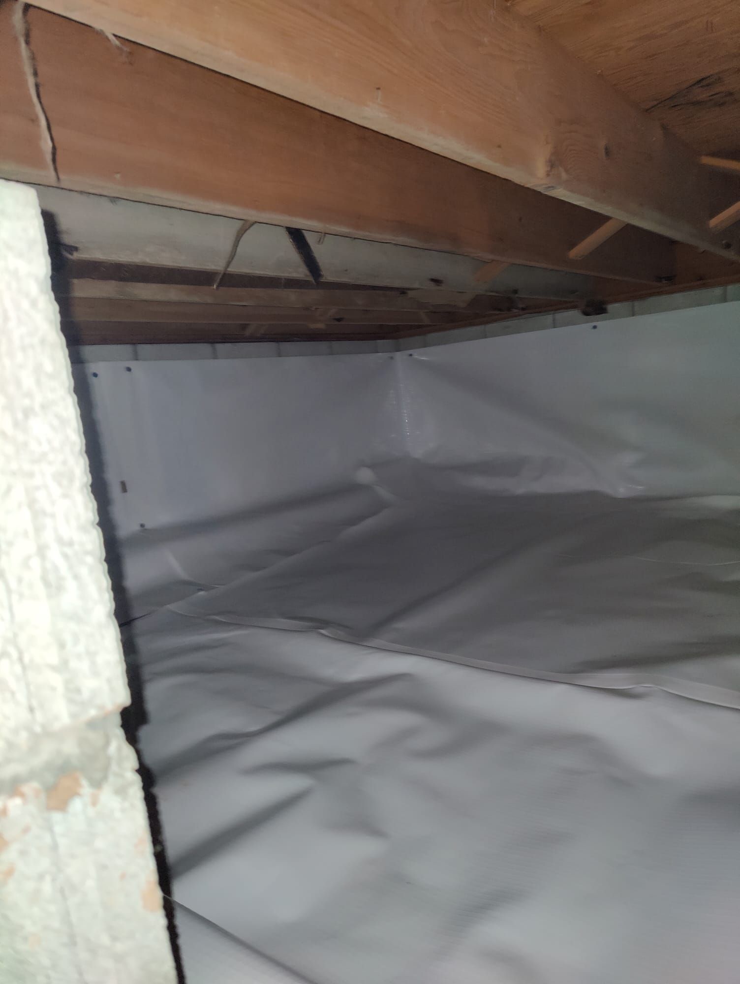 A basement with a white tarp on the floor and a wooden ceiling.