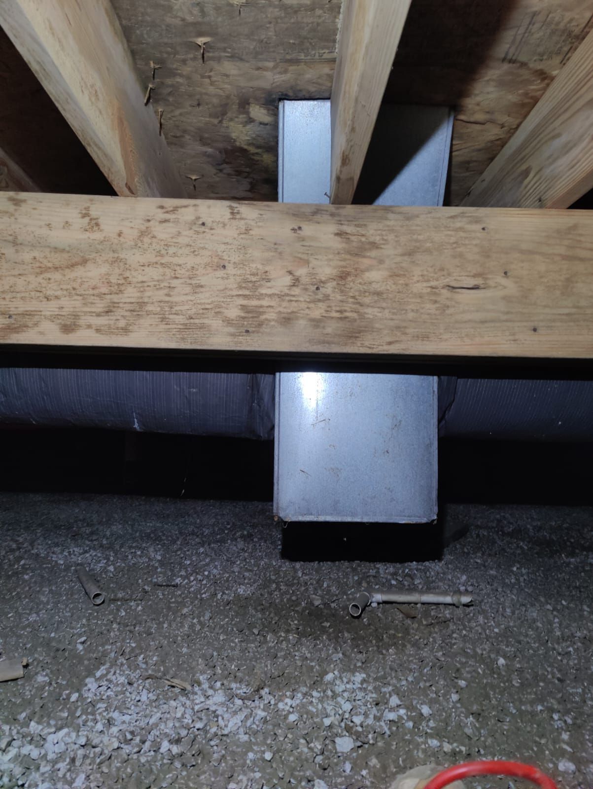 A wooden beam is sitting under a metal pipe in a basement.