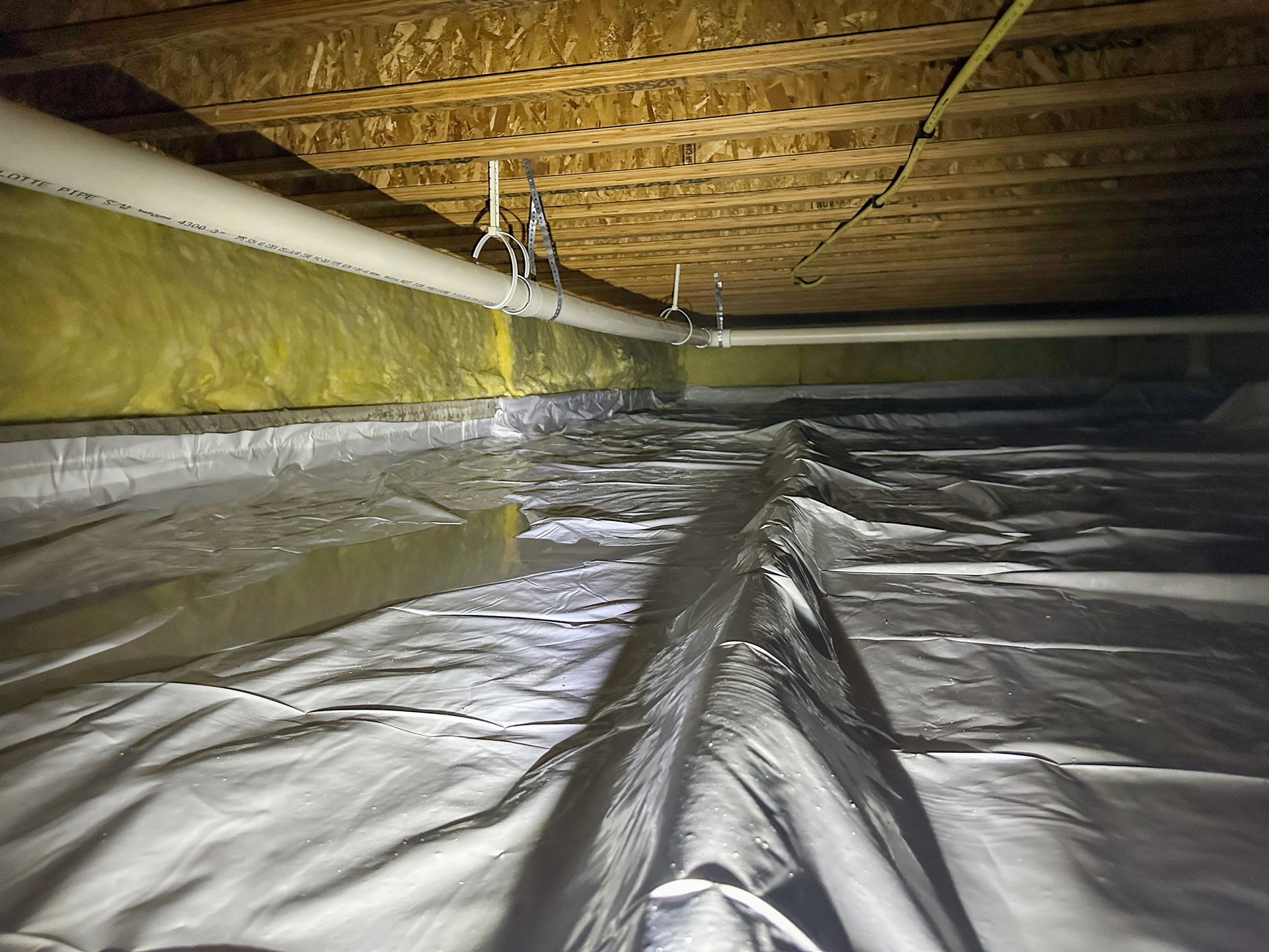 A crawl space with a lot of aluminum foil on the floor.