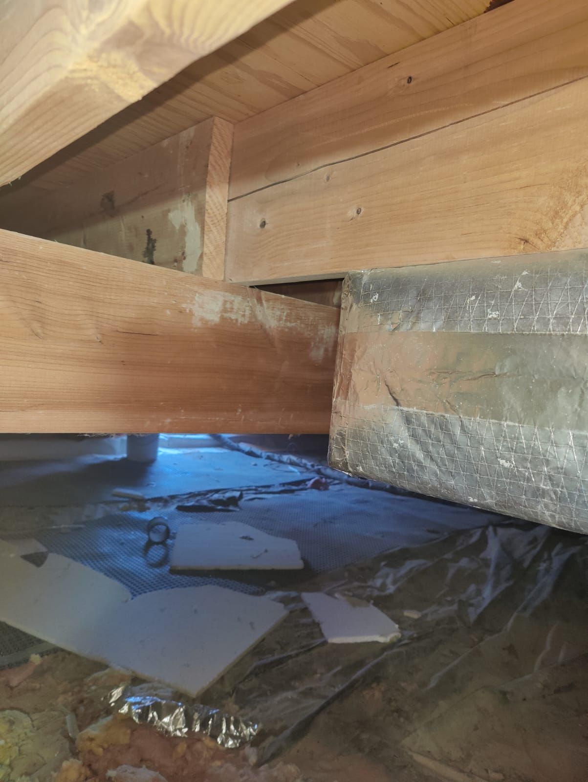 A wooden beam is sitting under a metal pipe in a basement.