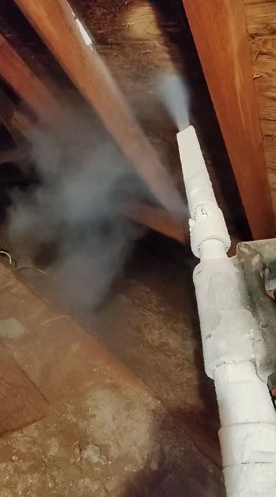 Smoke is coming out of a pipe in an attic.