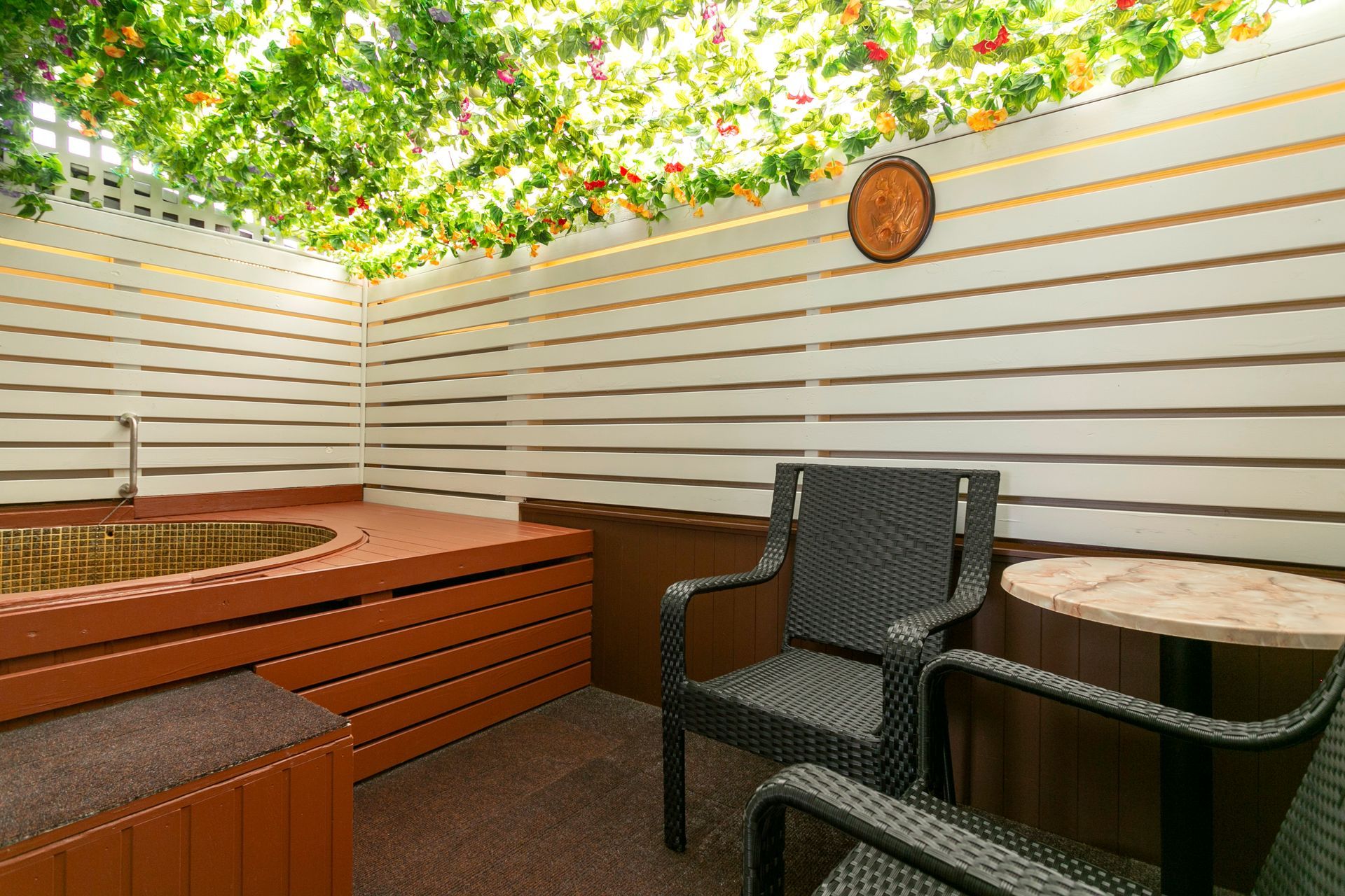A room with a jacuzzi , chairs , a table and a clock on the wall.