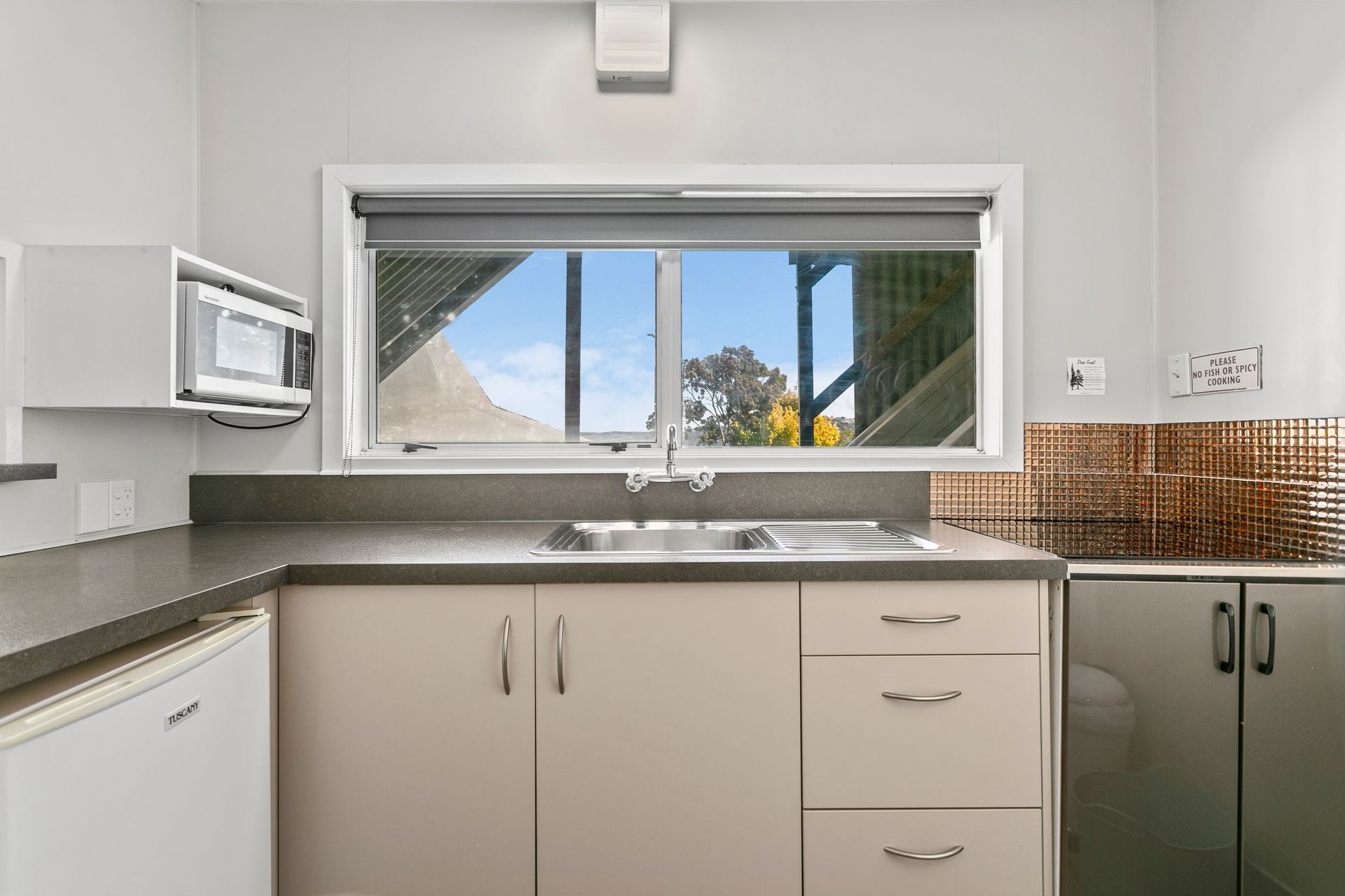 A kitchen with a sink , cabinets , a microwave and a window.