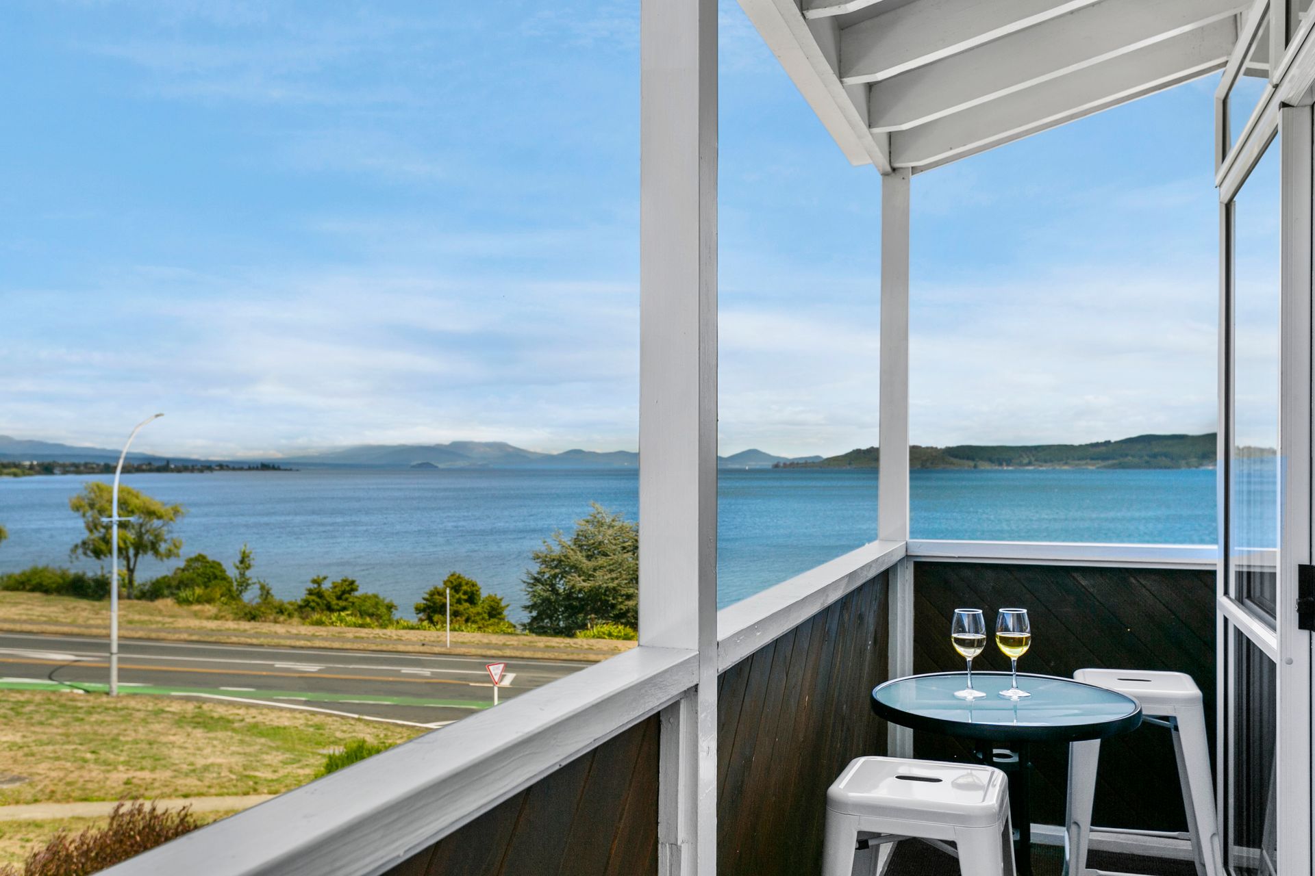 A balcony with a table and two glasses of wine overlooking a body of water.