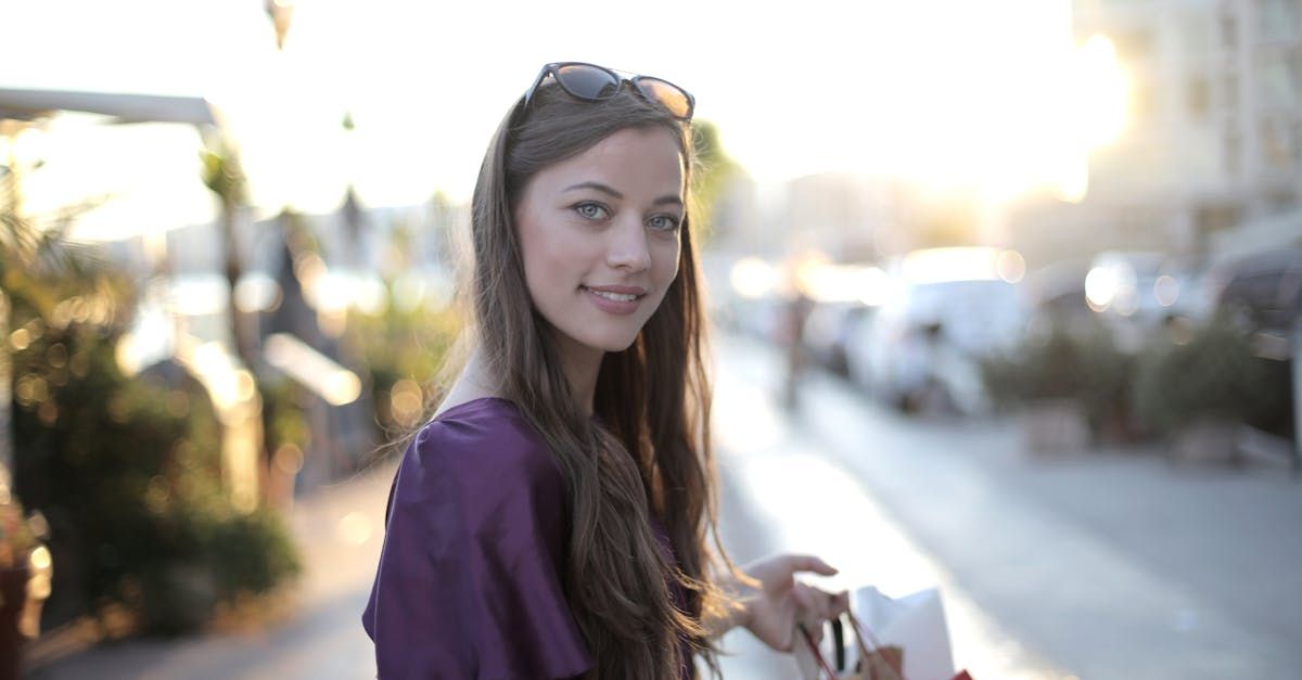 A woman is walking down a street holding a bag and smiling at the camera.