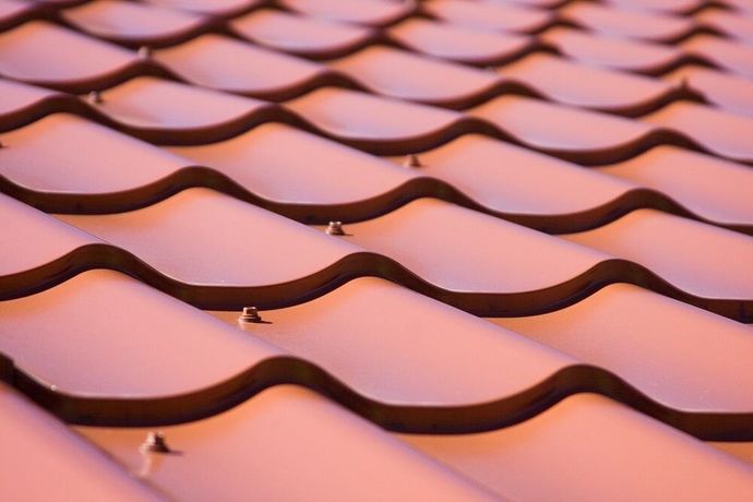 A close up of a pink tile roof with waves and screws — Bradshaw Plumbing & Roofing Pty Ltd In East Mackay, QLD