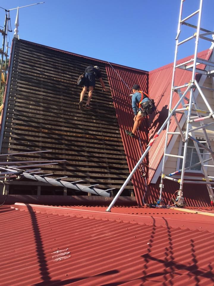 Two Men Are Working on the Roof of a Building — Bradshaw Plumbing & Roofing Pty Ltd In East Mackay, QLD