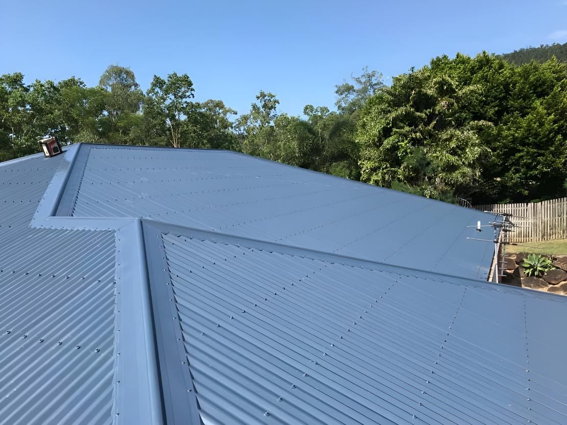 A Blue Corrugated Metal Roof With Trees in the Background — Bradshaw Plumbing & Roofing Pty Ltd In East Mackay, QLD A Blue Corrugated Metal Roof With Trees in the Background — Bradshaw Plumbing & Roofing Pty Ltd In East Mackay, QLD