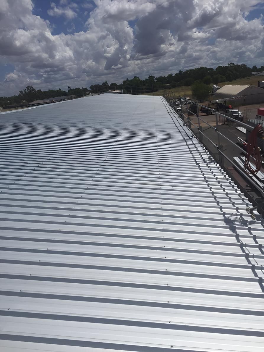 A Large Metal Roof With a Blue Sky in the Background — Bradshaw Plumbing & Roofing Pty Ltd In East Mackay, QLD A Large Metal Roof With a Blue Sky in the Background — Bradshaw Plumbing & Roofing Pty Ltd In East Mackay, QLD