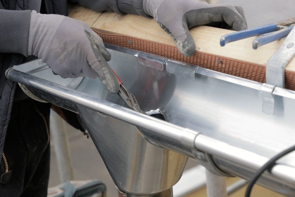 A Person is Working on a Metal Gutter With a Pair of Pliers — Bradshaw Plumbing & Roofing Pty Ltd In Marian, QLD A Person is Working on a Metal Gutter With a Pair of Pliers — Bradshaw Plumbing & Roofing Pty Ltd In Marian, QLD