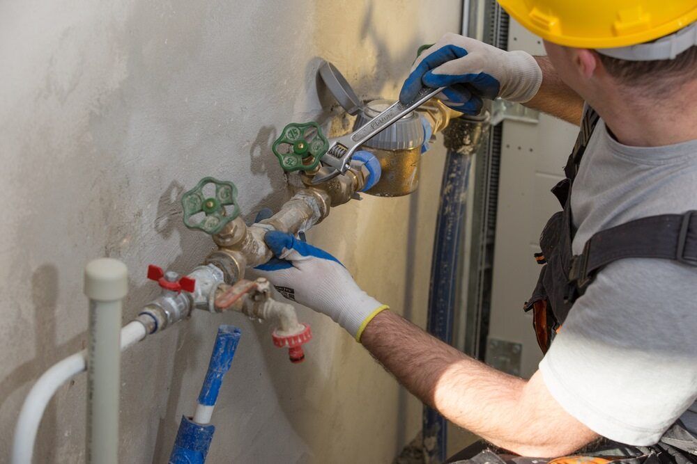 A Man is Fixing a Water Pipe With a Wrench — Bradshaw Plumbing & Roofing Pty Ltd In Ooralea, QLD A Man is Fixing a Water Pipe With a Wrench — Bradshaw Plumbing & Roofing Pty Ltd In Ooralea, QLD