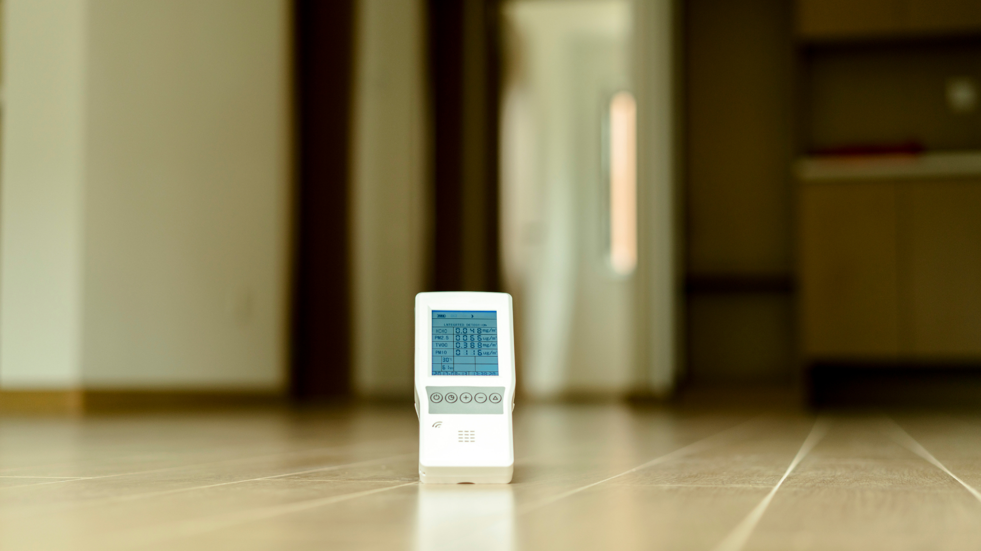 A digital thermometer is sitting on the floor in an empty room.