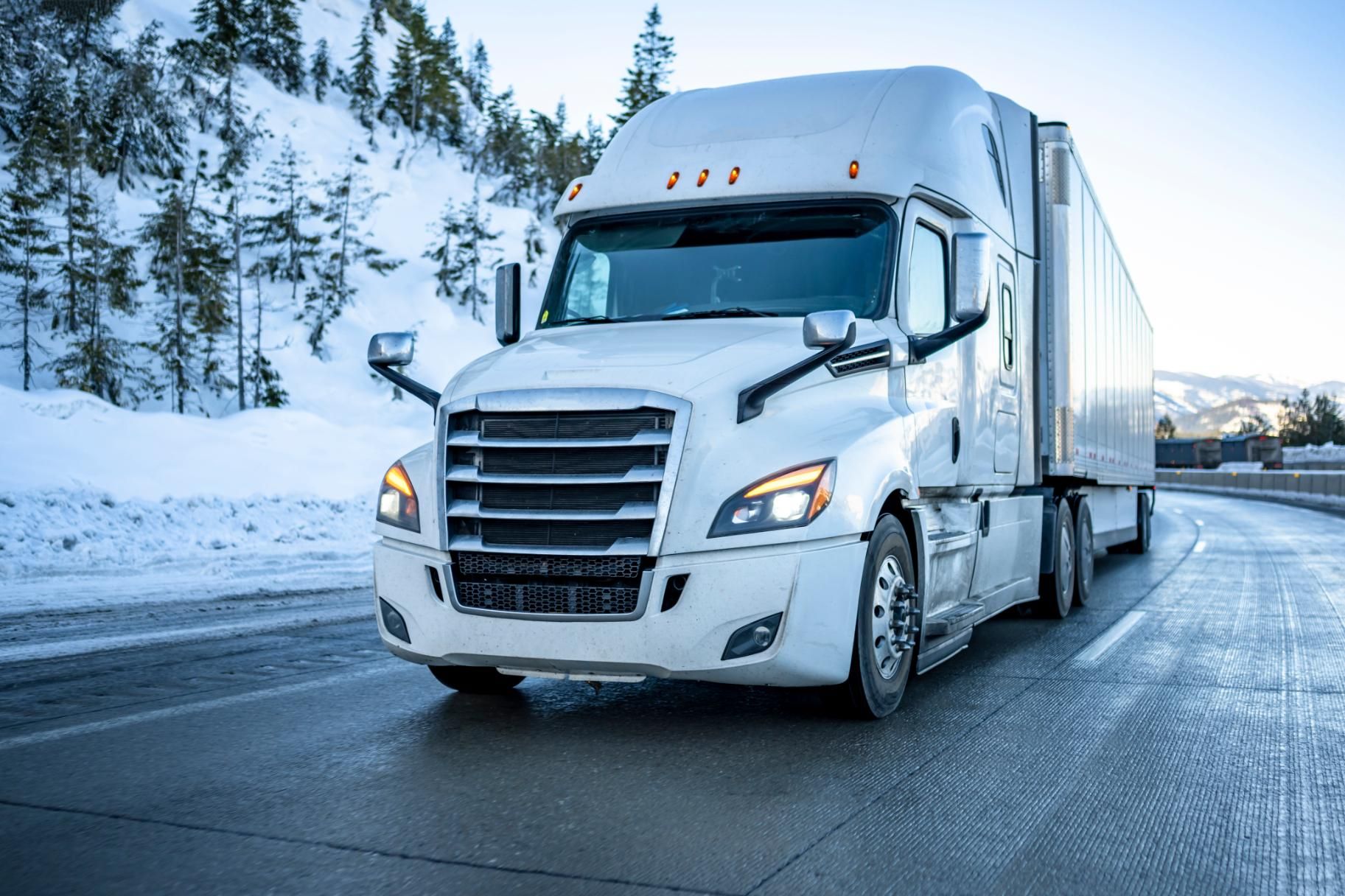 A white semi truck is driving down a snowy highway.